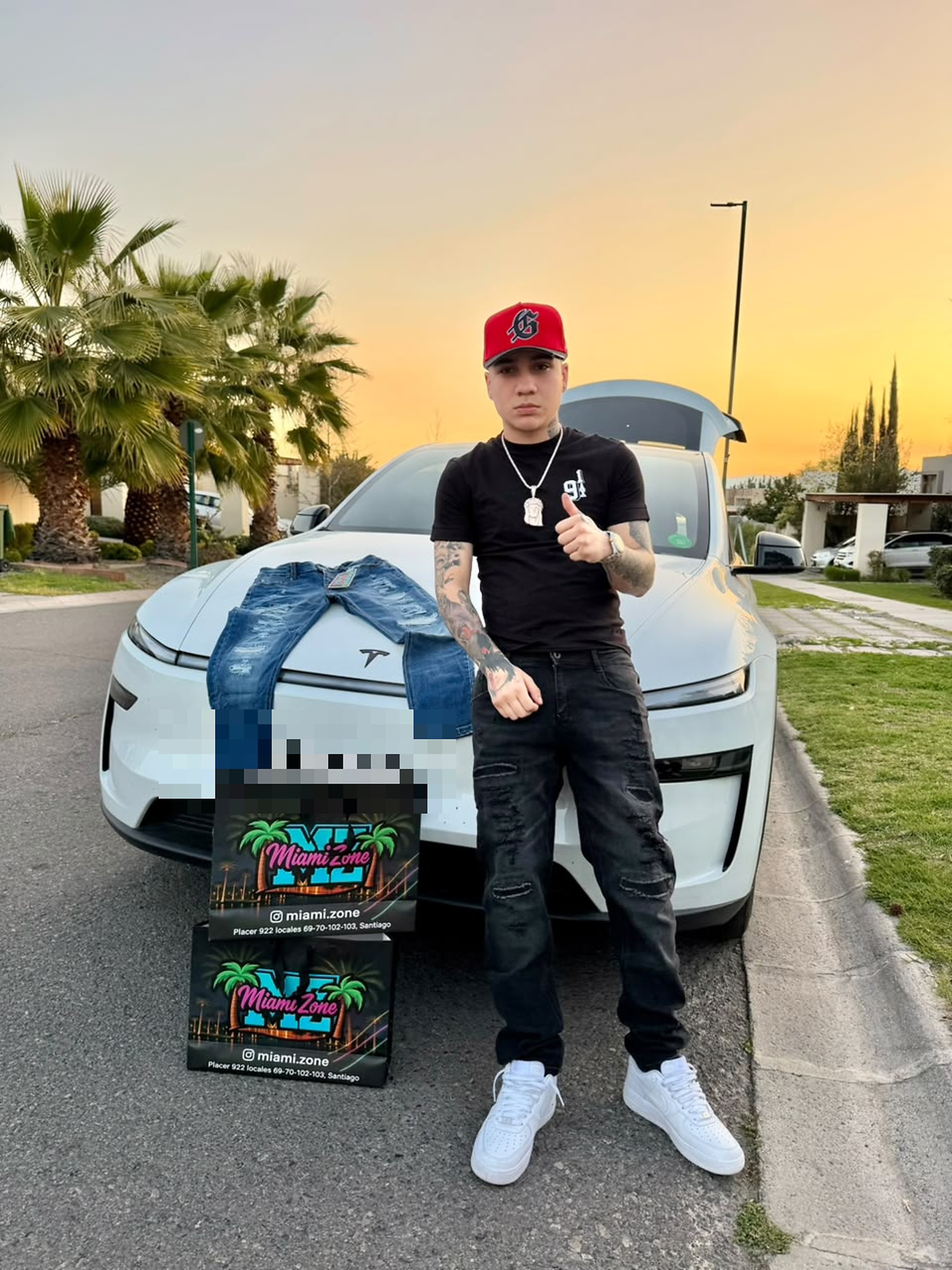 Cantante urbano frente al atardecer, jeans Miami Zone colgados sobre el capó y bolsas MZ